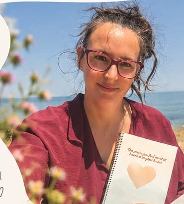 Ellen zit in het gras bij zee, met een notitieboek met een hart erop