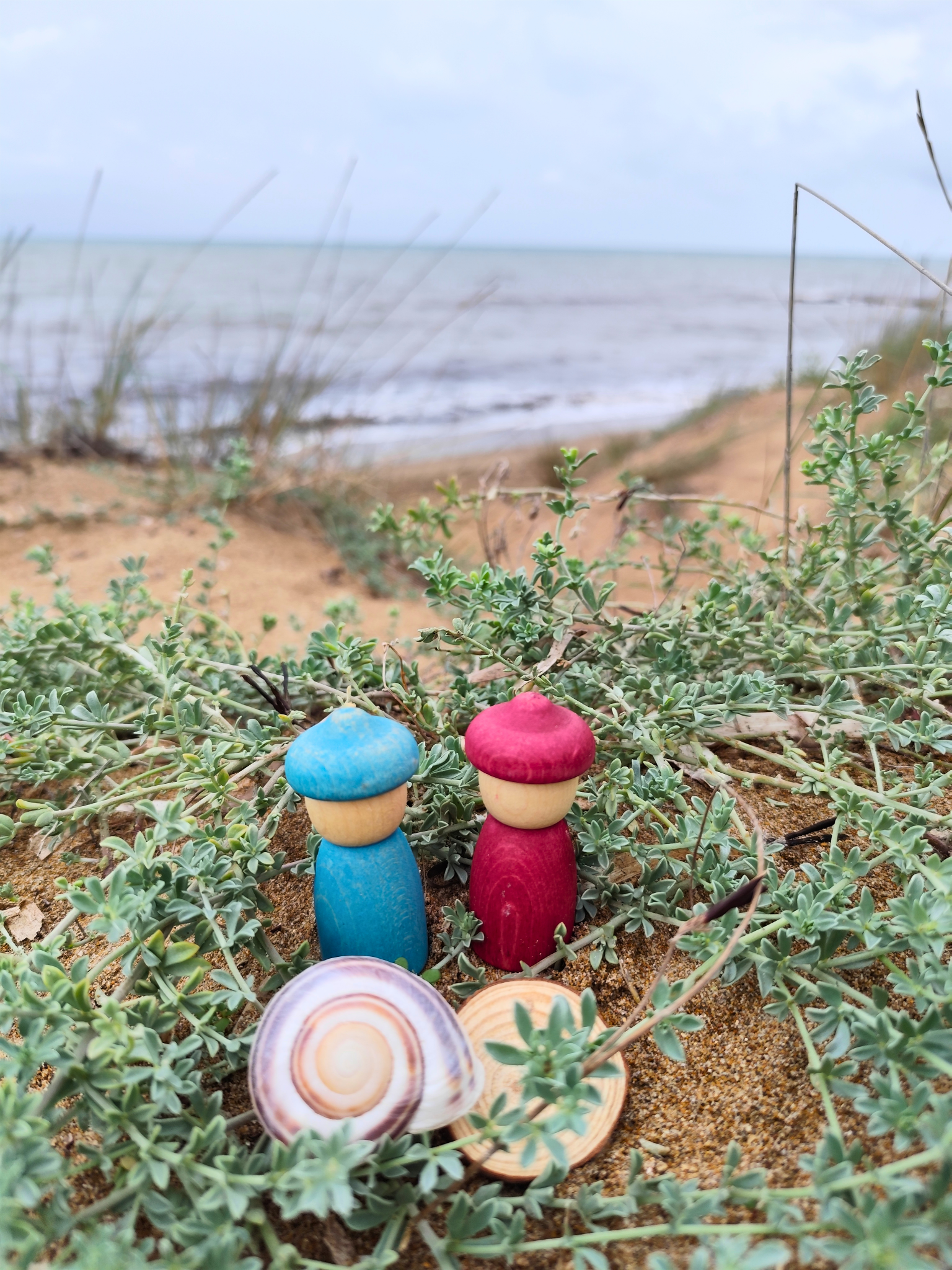 2 houten poppetjes en slakkenhuisje in de duinen aan het strand. 